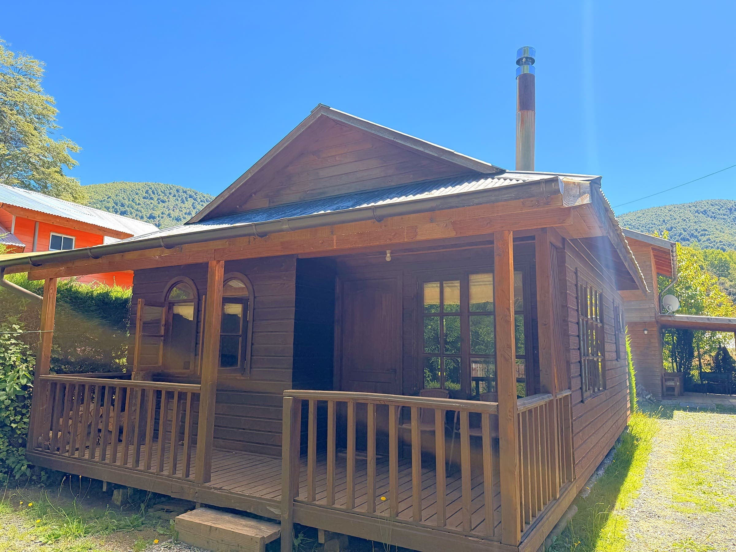 Cabaña de madera de un piso con terraza techada y cielo azul, en Caburgua